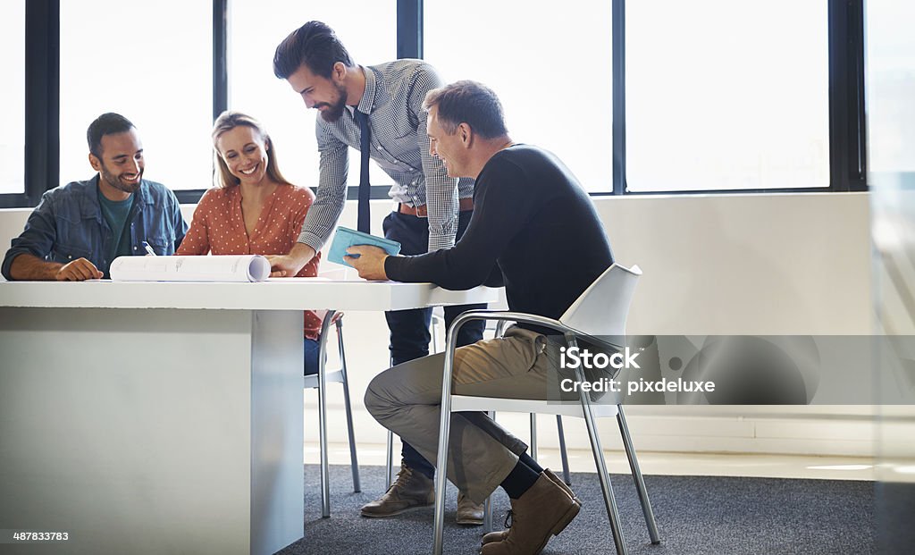 Group of coworkers discussing plans Shot of four coworkers going over a set of plans together Adult Stock Photo