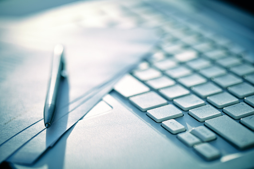 Close-up of computer keyboard with paper and pen on it