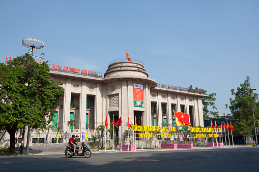 Hanoi, Vietnam - August 23, 2015: Motorcycle traveling in front of the building of The State Bank of Viet Nam in Hanoi capital. The State Bank of Vietnam is the central bank of Vietnam and known as the Indochina Bank in the past.