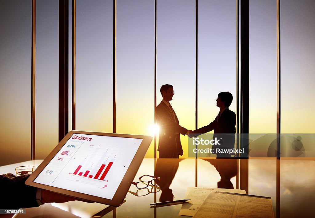 Silhouettes Of Two Businessmen Shaking Hands Together Silhouettes Of Two Businessmen Shaking Hands Together In A Board Room Graph Stock Photo