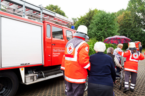 Bochum, Germany - September 14, 2013: Capture of Red Cross members in operation guiding senior people of nursing home out of danger zone. They are passing fire engine. Scene is part of evacuation training made by Red Cross and fire fighters of Bochum. Shot is part of serie taken for Red Cross.