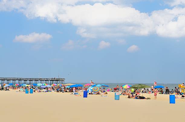 Ocean City, Maryland, USA - July 2, 2009: A large group of tourist visit the Ocean City beach, the crowd include families, teens, adults and children. It is a multi-racial group having fun at the beach on a bright summer day. The Ocean City fishing pier is in the background with many people trying their luck with the local fish. as a gull wheels overhead looking for a handout.