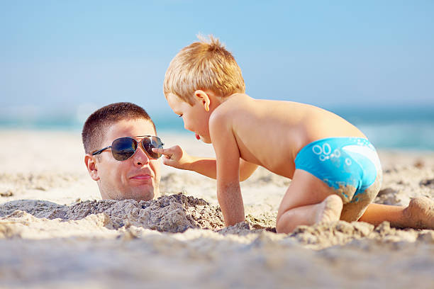father and son having fun in sand on the beach father and son having fun in sand on the beach burying stock pictures, royalty-free photos & images
