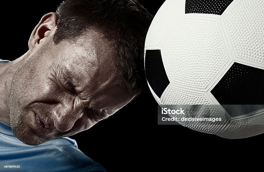 Header! Close up of a Caucasian male soccer player heading a football aganst a black background. With grainy photoshop effect. Soccer Stock Photo