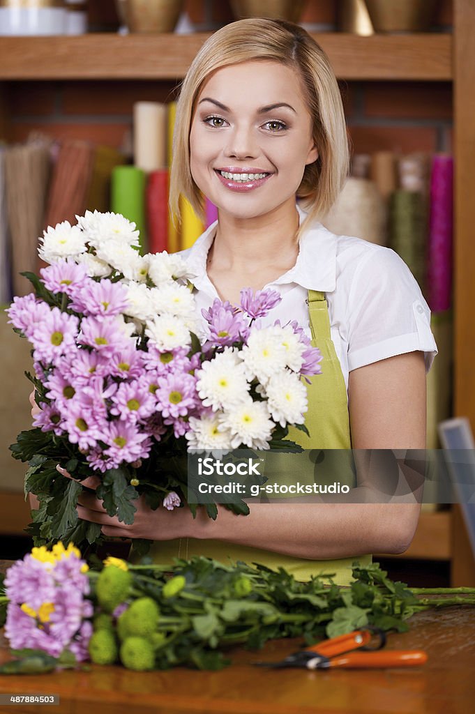 Making a beautiful flower bunch. Beautiful young blond hair woman in apron arranging flowers and looking at camera Adult Stock Photo