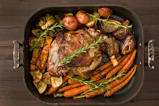 An overhead close up shot of a roasted leg of lamb and vegetables garnished with rosemary  twigs.