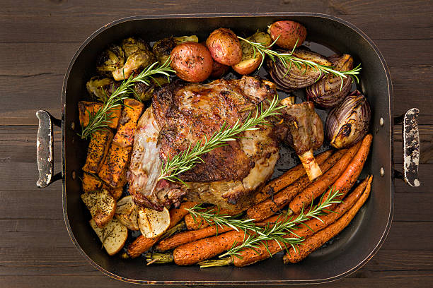 Roasted Leg Of Lamb And Vegetables An overhead close up shot of a roasted leg of lamb and vegetables garnished with rosemary  twigs. lamb meat stock pictures, royalty-free photos & images