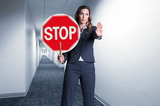 A businesswoman standing in a long hallway holding a stop sign.