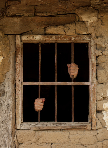 human hands holding prison bars