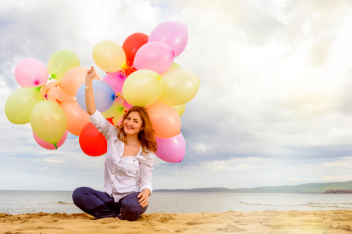 happy woman on beach with colorful balloons smiling at camera.