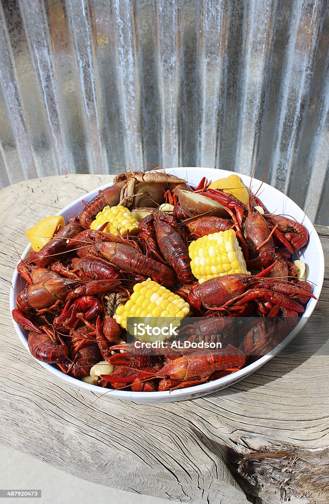 Crawfish Boil Plated on Rustic Wood Table Crawfish boil with corn, potatoes and garlic, on a white plate.  Sitting on a rustic old wood table.  Corrugated metal background. Corn Stock Photo