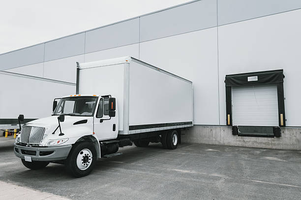 Delivery Trucks at Warehouse Delivery and semi trucks are loaded at a warehouse in an industrial park. loading bay stock pictures, royalty-free photos & images