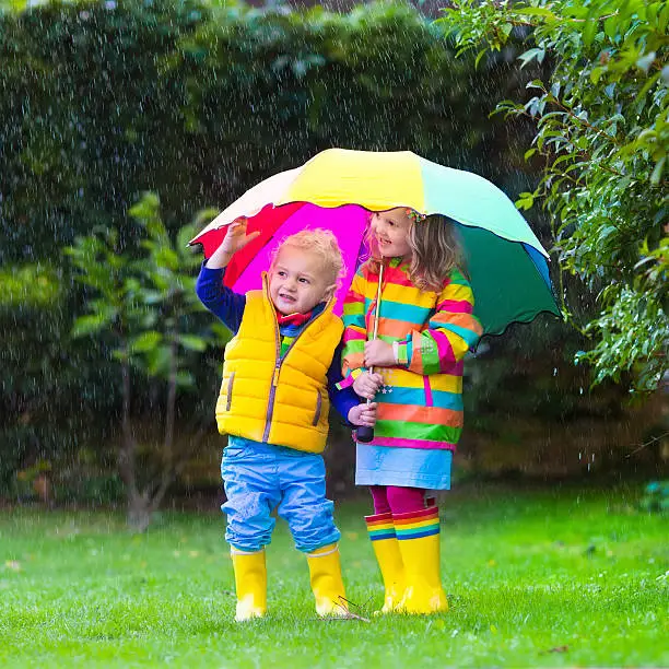 Photo of Kids playing in the rain under colorful umbrella