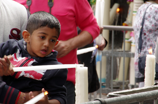 Lourdes, France - August 19, 2015: Little boy is  light up a candle during a prayer ceremony. A lot of people where present. 