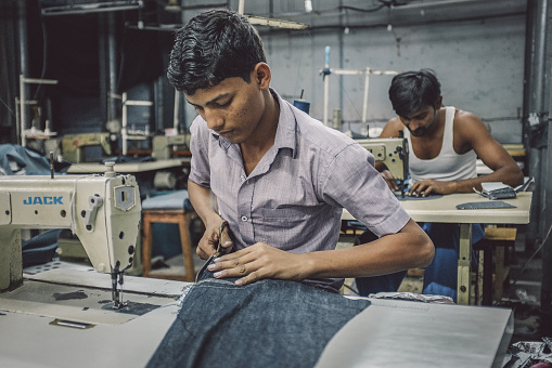 Mumbai, India - January 12, 2015: Indian workers sew in clothing factory in Dharavi slum. Post-processed with grain, texture and colour effect.