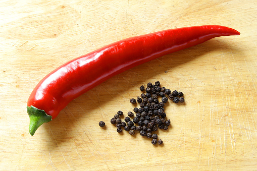 long red hot pepper shiny on kitchen board with dried black peppers