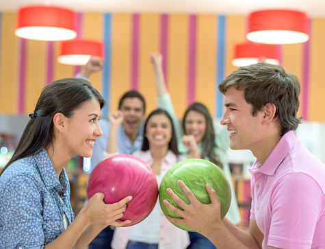 Competitive man and woman bowling with their teams at the background and challenging each other