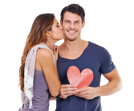 Studio shot of a young woman kissing her boyfriend who is holding a heart