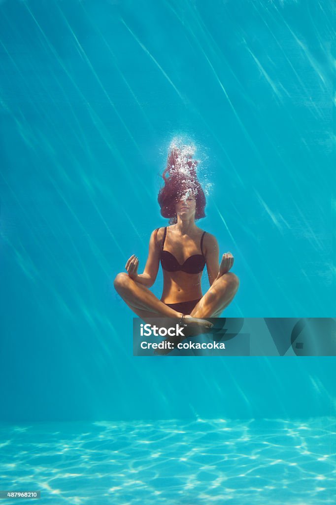 underwater meditation young woman in black bikini in yoga position underwater in diving aquarium, full body shot, front view through the glass Swimming Pool Stock Photo