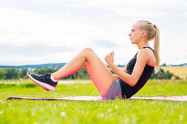 молодая женщина, делая sit ups в парке - sports training sit ups moving up sitting стоковые фото и изображения
