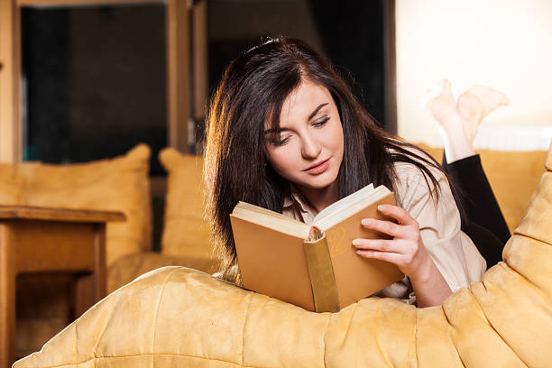 istock Woman lying on her couch reading a book at home 487971848