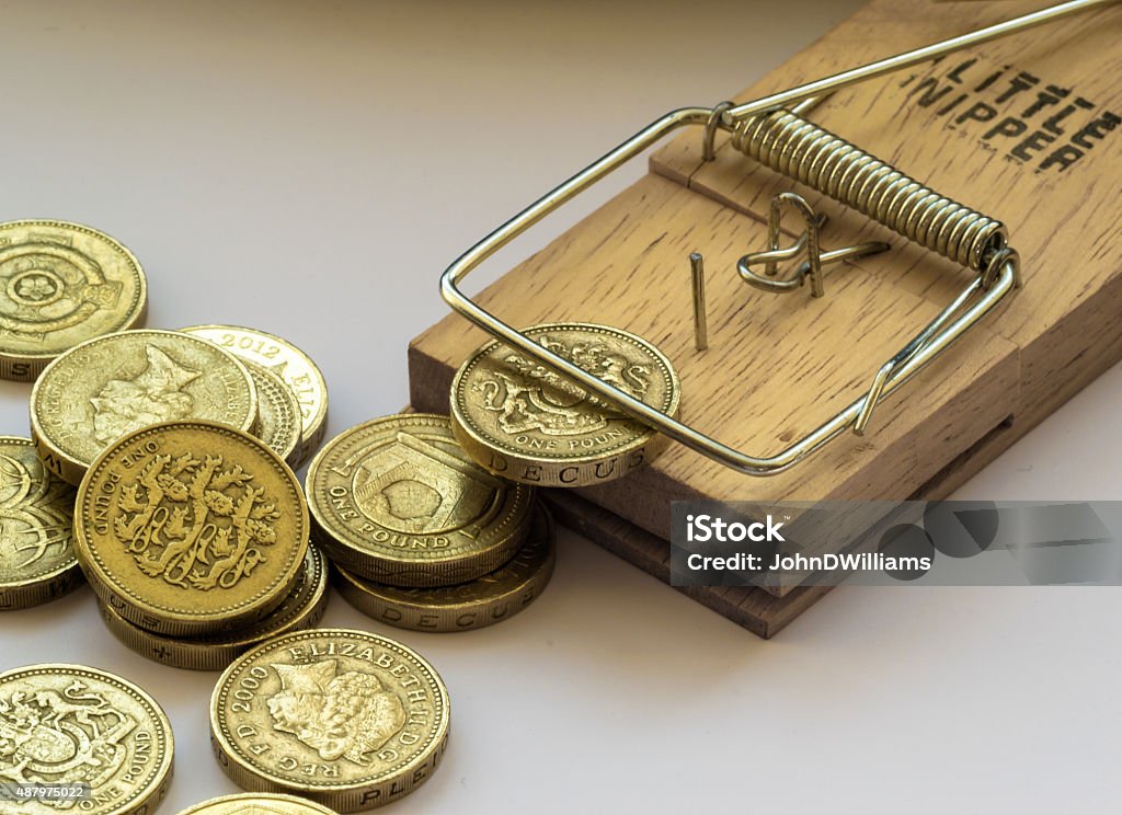 Mouse Trap Catches a British Pound Coin Single mousetrap in macro on a white background catches and traps a British pound coin as other coins await their turn 2015 Stock Photo