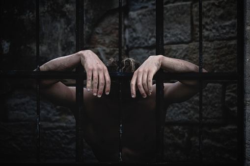 A man hanging depressed on the bars of a prison cell. Evokes emotion and conceptual feelings about prison.