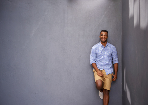 A handsome young man leaning against a gray wall