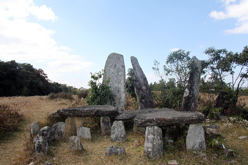 Several standing stone megaliths stand on the hillside with Mawphlang sacred forest behind in Meghalaya, India