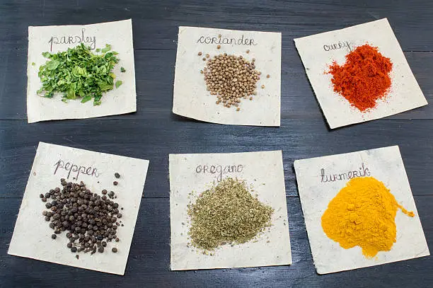 Various spices  on recycled papers with labels placed  on a dark wooden table