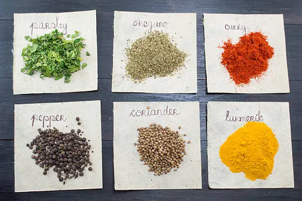 Various spices  on recycled papers with labels placed  on a dark wooden table