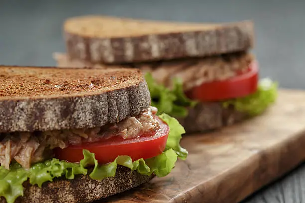 closeup photo of sandwich with tuna and vegetables on rye bread on wood background