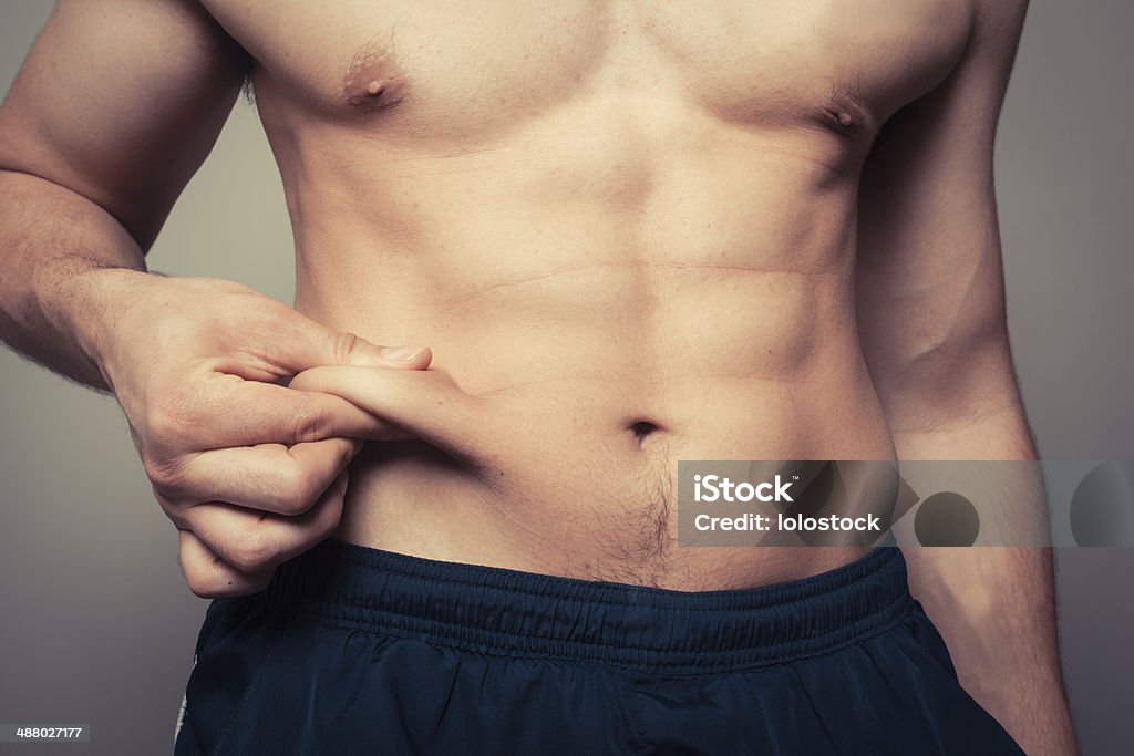 Fit young man pinching his stomach Fit young man pinching the fat on his stomach Liposuction Stock Photo