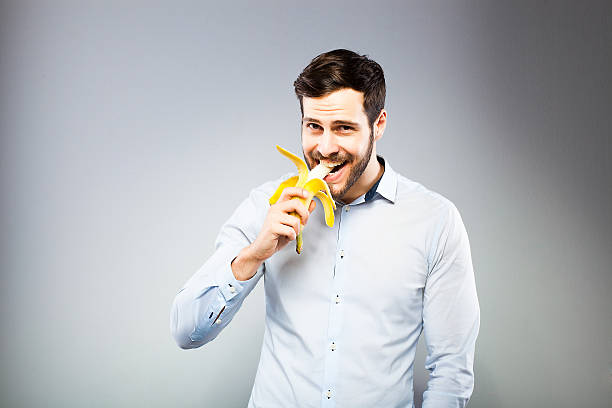 Portrait of a smart serious young man eating banana stock photo