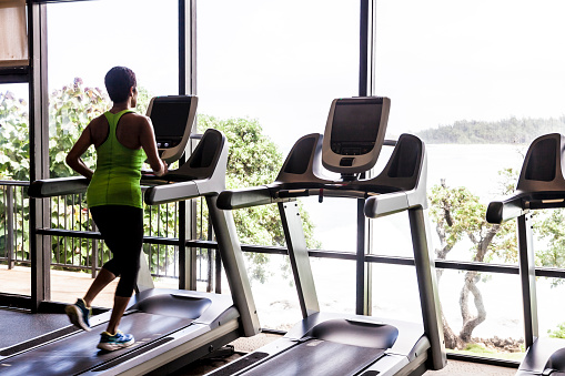 Woman Exercising in Gym running on treadmill with view to tropical ocean