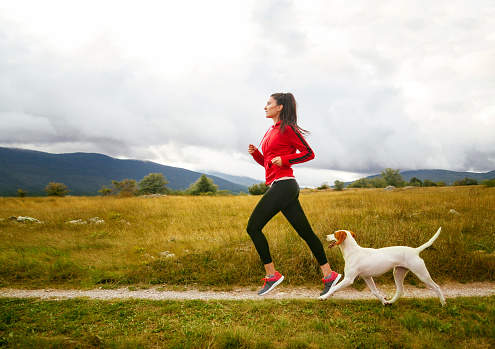 Young woman jogging through the countryside with her pet dog. Taken on a rainy day, under the cloudy sky. 