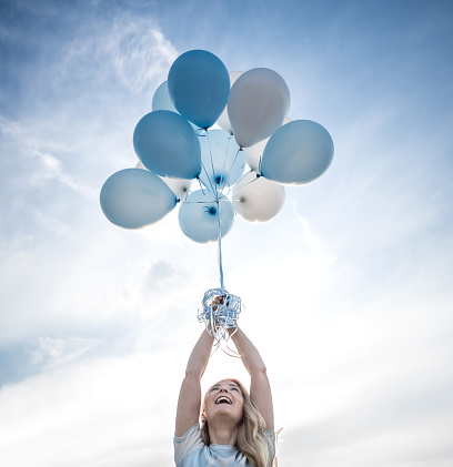 Beautiful woman holding a bunch of helium balloons outdoors about to launch them in the sky