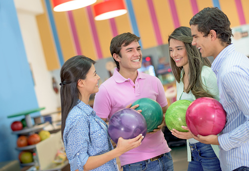 Group of friends having fun bowling and holding balls while looking very happy