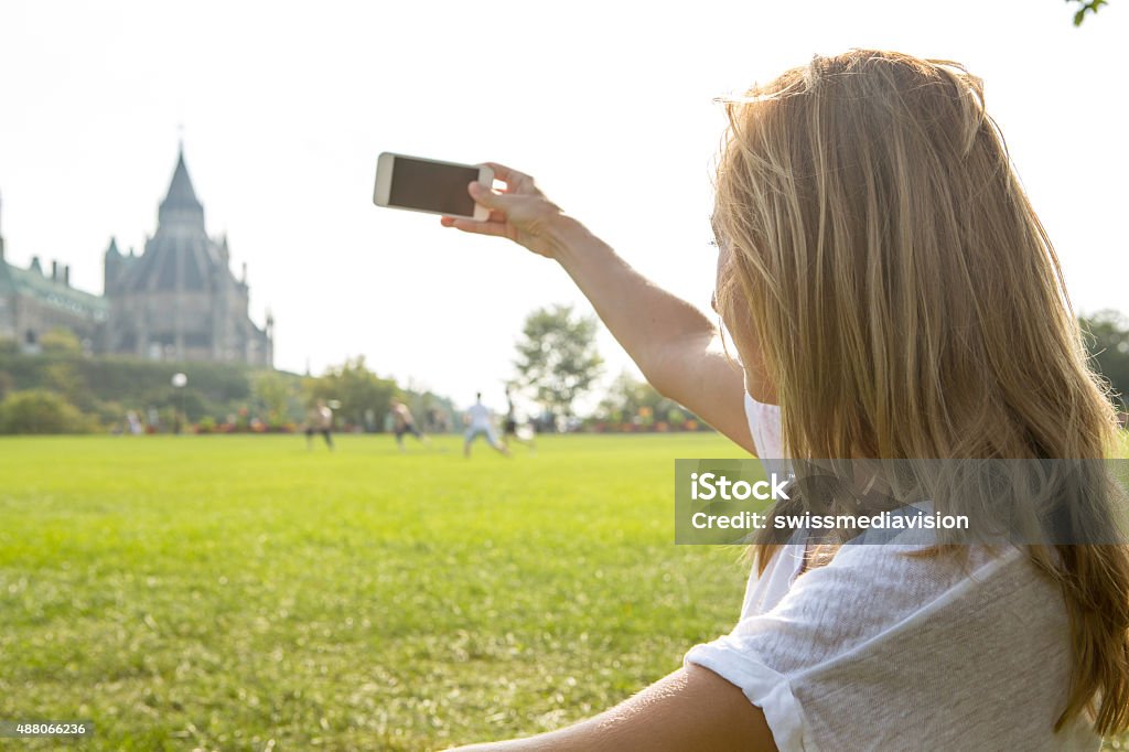 Young woman in Ottawa photographing parliament using mobile phone Young cheerful woman in Ottawa-Canada taking a photo of the parliament building using her mobile phone.  20-29 Years Stock Photo
