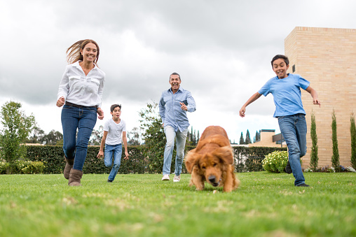 Latin American family running outdoors with the dog at the park - go fetch concepts