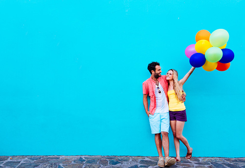 Happy couple with multi coloured balloons against blue wall