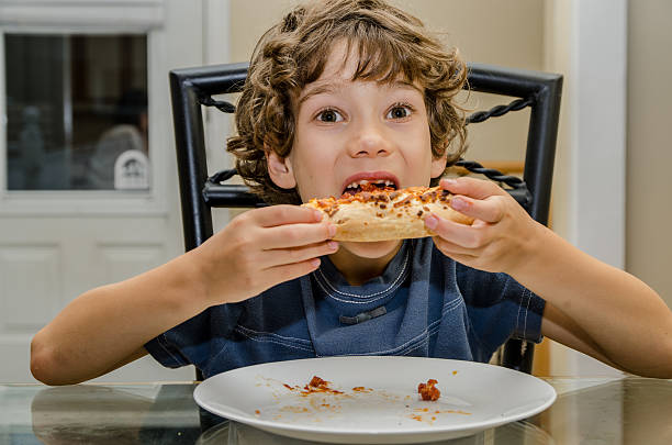 istock Boy eating slice of pizza in white plate 488080300