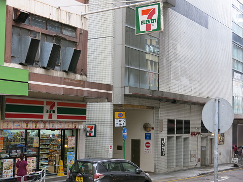 Hong Kong, Hong Kong S.A.R. – August 14, 2015: A view of sidewalk in Hong Kong. 7-11 Convenience Store on the sidewalk. Pedestrians walk past the store. Cars are on the road. 
