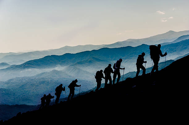 Silhouette of Hikers At Dusk Silhouettes of hikers climbing the mountain at Dusk climbing up a hill stock pictures, royalty-free photos & images