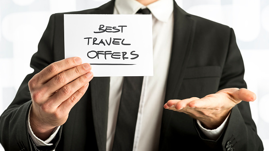 Close up Businessman Holding Small Paper with Best Travel Offers Message Against White Background.