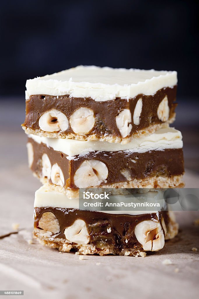 Caramel, white chocolate and nuts squares Millionaire shortbread bars with caramel, whute chocolate, raisins and hazelnuts on a wooden background Bar - Drink Establishment Stock Photo