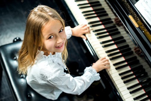 High angle view of smiling little girl practicing and playing piano and looking at camera.