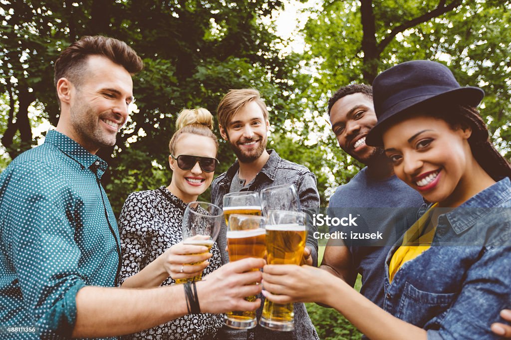 Multi ethinc friends toasting with beer outdoors Multi ethnic group of happy friends - caucasian and afro american - toasting with beer glasses outdoors, laughing at camera. Beer Glass Stock Photo