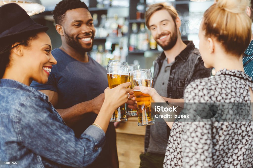 Friends toasting with beer in a pub Excited multi ethnic group of friends - caucasian and afro american - toasting with beer glasses in the pub. Drinking Stock Photo