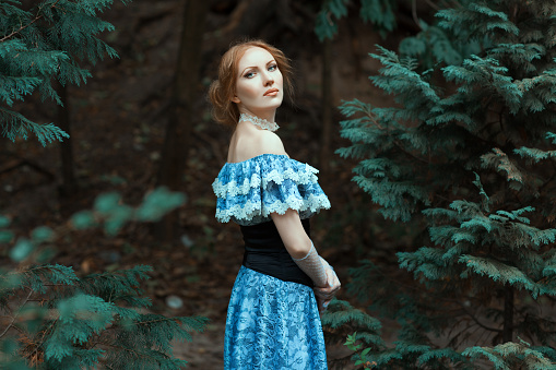 Girl dressed in an old-fashioned blue dress. She walks in the park among the trees.